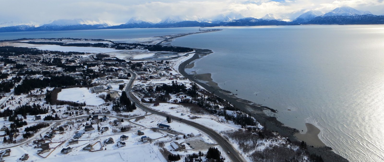 Aerial view of Homer, Alaska, in winter, with snowy streets and homes along the shore of Kachemak Bay and the Homer Spit reaching out behind.